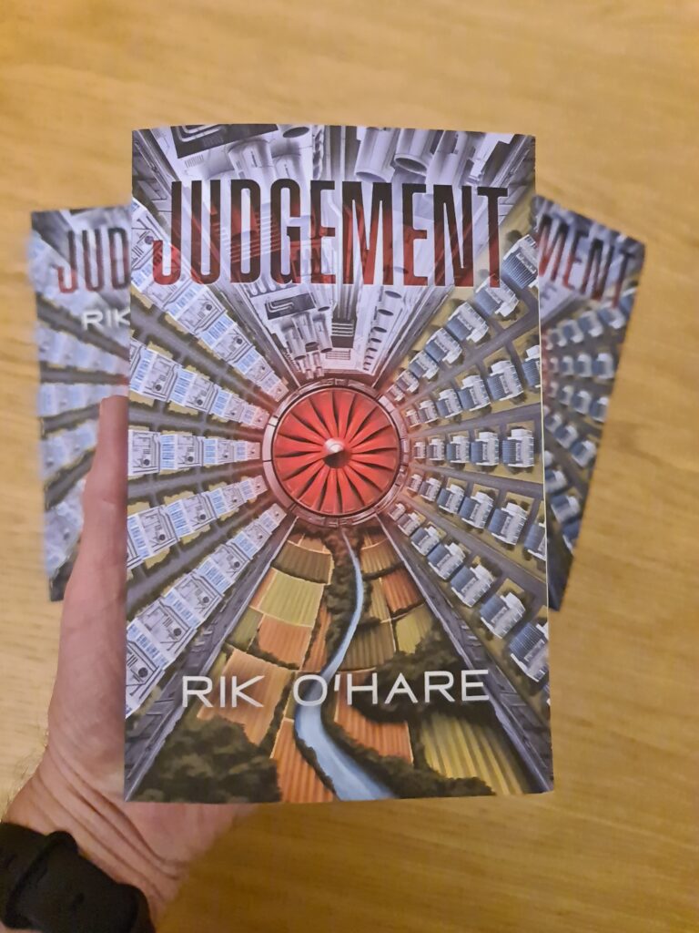 An authors hand holding a physical copy of their science fiction novel called Judgement